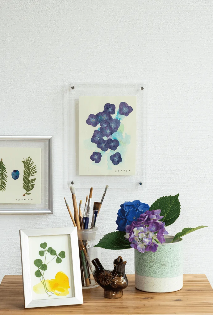 写真：木のテーブルに飾られた押し花のアート作品と、紫陽花、絵筆。