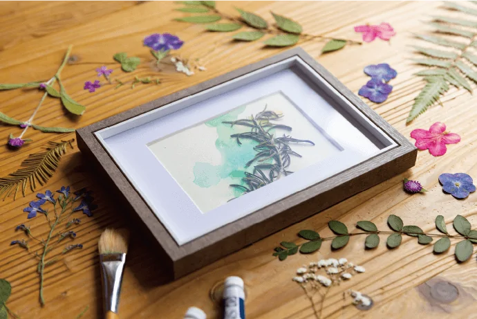 写真：木のトレイに納めた押し花のアート作品と、テーブルに並べた色とりどりの押し花。
