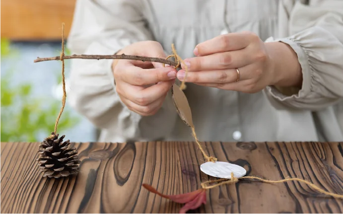 写真：小枝に麻ひもを結びつけて、オーナメントを作っている手元。