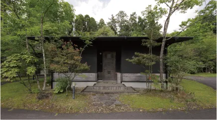 木々に囲まれた小さな黒い建物と落ち着いた庭の風景です。